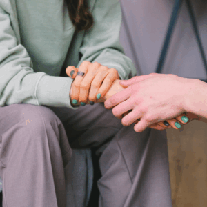 Two people's hands clasped together in a comforting gesture at a grief support group event.